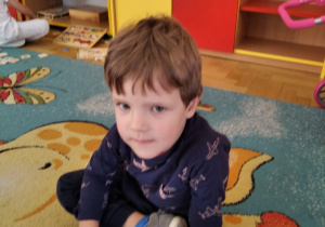 Chłopczyk siedzi na dywanie.